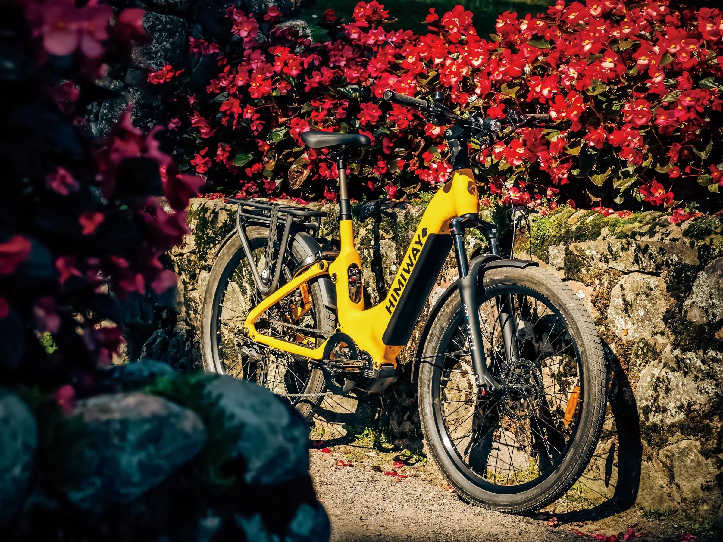 Yellow bicycle leaning against a stone wall with red flowers in the background